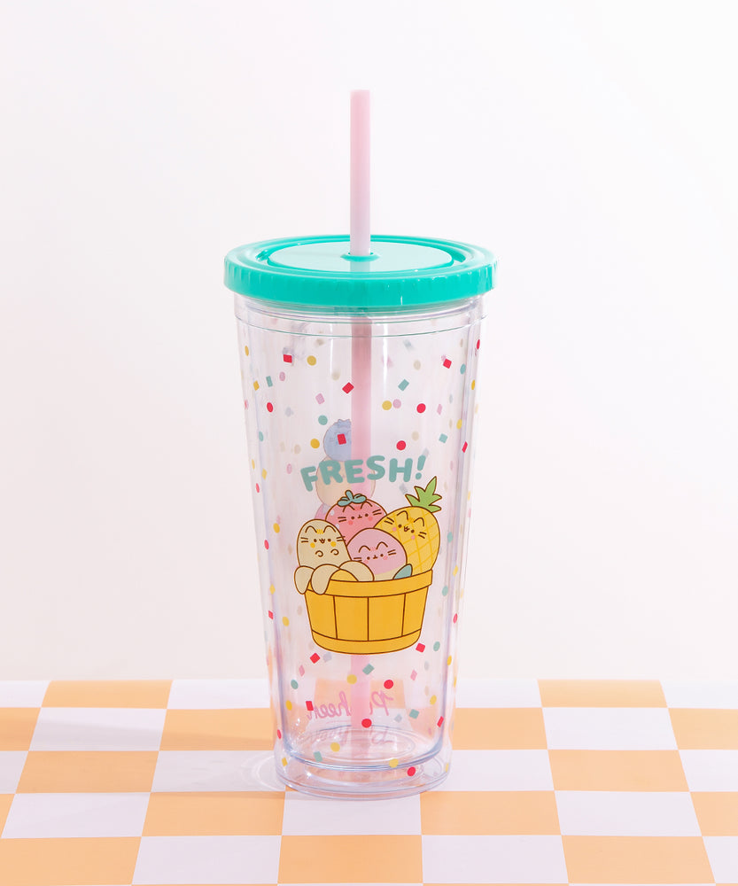 Front view of the Pusheen Fruits Tumbler. The clear beaker has a confetti print all over the clear base. The graphic on the front of the tumbler features Pusheen as a Banana, Peach, Strawberry, and Pineapple tucked inside a basket.