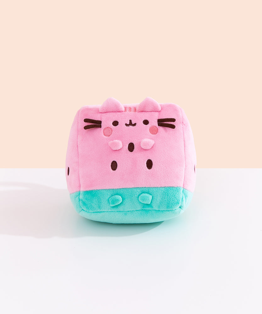 Front view of the Pusheen Fruits Watermelon Plush. Pusheen the Cat takes the form of a triangular watermelon slice. The pink and green plush sits atop a white tabletop. 