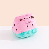 Side quarter view of the plush. The plush sits upright while Pusheen’s four paws extend off the front of the plush and do not touch the tabletop surface the plush is sitting on. The brown embroidered spots on the sides and front of the plush mimic watermelon seeds. 