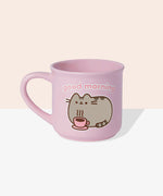 Front view of the Pusheen Good Morning Mug. The rounded light-pink mug is perfect for all hot beverages. The exterior has a light-pink handle with matching interior walls. The outside of the mug features Pusheen the Cat laying down with her own hot beverage and the saying “Good Morning” above the cat graphic.  