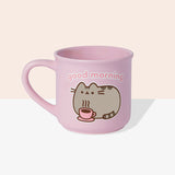 Front view of the Pusheen Good Morning Mug. The rounded light-pink mug is perfect for all hot beverages. The exterior has a light-pink handle with matching interior walls. The outside of the mug features Pusheen the Cat laying down with her own hot beverage and the saying “Good Morning” above the cat graphic.  