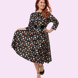 Alternate model shows off the print of the Pusheen Halloween Dress by holding the skirt out to her right side. The pattern extends from the boat neckline to the dress hem. 