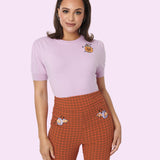 Model wears Pusheen Halloween Knit Sweater paired with Pusheen Halloween Pants. The lavender sweater is short sleeved with slightly puffed sleeves. On the wearer’s left side chest features an embroidered graphic of Pusheen the Cat sitting inside a Jack-O-Lantern surrounded by five black stars. 