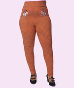 Front view of the orange, black, and purple Pusheen-themed Halloween pants. The orange pants have black plaud lines. The skinny, high-waisted pant silhouette has two embroidered graphics of Batsheen on the wearer’s hips. 