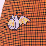 Close-up of bat embroidery on wearer’s hips. Pusheen takes the form of a purple bat pointing towards the inside of the pants. Her wings are purple and orange striped and she is surrounded by five black stars. 