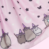 Closeup view of the printed pattern on the Pusheen Halloween Skirt. Witch Pip, Witch Pusheen, and Witch Stormy sit ready for spooky while wearing purple hats. The cats are surrounded by black bats and stars, and white sparkles, crescent moons, and sparkles.  