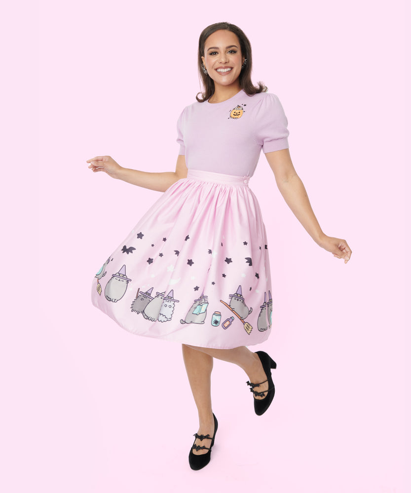 Model wears the Pusheen Halloween Skirt paired with the Pusheen Halloween Sweater. The model spins to show a full view of the repeating pattern on the middle and hem of the skirt. The light pink fabric has graphics of grey Witch Pusheen, Witch Pip, and Witch Stormy.  