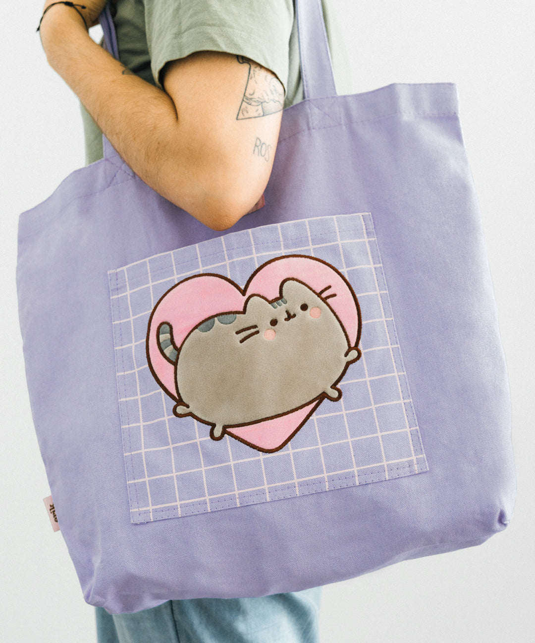 A model holds the Pusheen Heart Deluxe Tote Bag on shoulder to show the scale and size of the bag.  