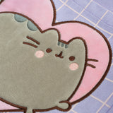 Close-up view of the Pusheen applique on the front pocket. The grey velour appliqué of Pusheen shows the cat blushing with surrounded by a heart and grid pattern.
