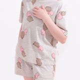 Model wears Pusheen Hearts Pajama Set. The two-piece loungewear set includes oversized grey top and elastic band shorts. Covering the top and shorts is a randomized pattern print of Pusheen and a light pink heart. 