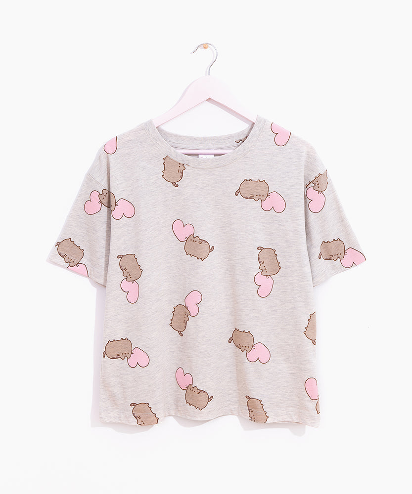 Hung on a white hanger, the Pusheen Pajama Tee is hung out to show the full length of the oversized t-shirt. The gray tee has printed all over graphic of Pusheen and pink hearts. 