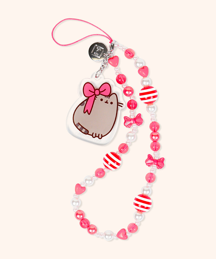 Holiday-themed beaded phone charm lies on a flat surface. The wristlet has red bow beads, red heart beads, white and red striped round beads, and white and red round beads. 