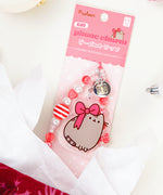 Beaded Phone Charm attached to backing packaging. The red and white paper card has the Pusheen logo on the top corner and says "beaded phone charm" on the front. 