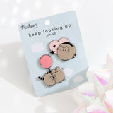 Two Pusheen pins are attached to a light blue backing card with the Pusheen Shop logo and the pin set name, “keep looking up pin set,” in a dark blue color. The pin set lies on a white background with a reflective white bow in the right corner. 