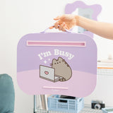 Model holds Pusheen Laptop Pad by attached carrying handle. The smooth top has a graphic of Pusheen the Cat with a laptop and the phrase "I'm Busy."