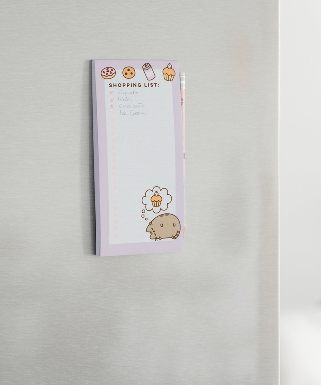 Pusheen Magnetic Shopping List hangs on a stainless steel fridge. The purple and white lined sheets feature graphics of Pusheen and sweet and savory treats. 