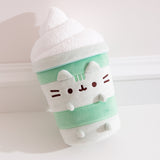 Close-up of Matcha Lattee Pusheen. The medium-green body is accompanied by light green horizontal lines to imitate a classic drink container. Pusheen's head stripes, eyes, smiling, mouth and whiskers are embroidered on the front of the plush while her light green ears and paws extend off the plush body.