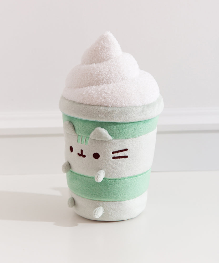 Left quarter view of the Matcha Latte Plush. The drink-inspired plush has a fuzzy whipped topping in a swirl pattern on top.