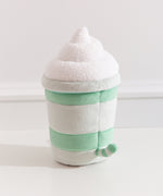 Back view of the Pusheen Matcha Plush. Pusheen's striped tail extends off the back of the drink-inspired plush. The cylinder base is topped with a fuzzy whipped plush topping.