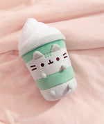 Pusheen Matcha Latte Plush lies on a plush pink blanket that highlights the soft green and white colors of the plush.