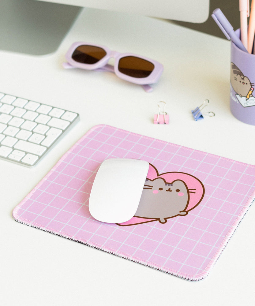 The pink with white grid pattern Pusheen Mouse Pad sits in front of its purple packaging. The packaging shows the size of the mouse pad as well as listing its features: waterproof, durability, precision, and speed. 