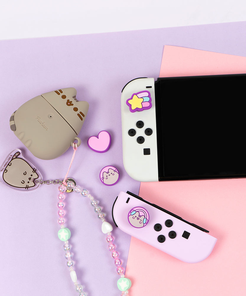 Pusheen Nintendo Switch Thumb Grip Caps placed on the controller poirtion of the Switch console. Next to the controller caps are Pusheen accessories including an AirPod case and Beaded Phone Charm.