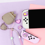 Pusheen Nintendo Switch Thumb Grip Caps placed on the controller poirtion of the Switch console. Next to the controller caps are Pusheen accessories including an AirPod case and Beaded Phone Charm.