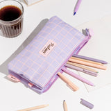 Pusheen case lies on its front on a desktop so the back of the bag can be seen. The purple bag has a light pink grid pattern background with the Pusheen the Cat logo in the center.