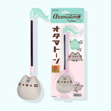 Pusheen Otamatone next to its packaging The mint green and pink packaging says "Otamatone," "Pusheen," and "FUN! Toy Musical Instrument."