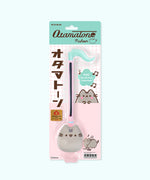 Pusheen Otamatone in its packaging. The printed cardboard backing card features three graphics of Pusheen the Cat next to the toy that is held in place by a clear plastic covering.