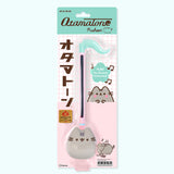 Pusheen Otamatone in its packaging. The printed cardboard backing card features three graphics of Pusheen the Cat next to the toy that is held in place by a clear plastic covering.