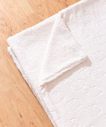 Close-up view of the cream sherpa-backed blanket. The polyester blanket is folded to show both sides of the blanket with the sherpa-baked side followed over to show the underside.  