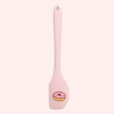 Close-up of included pink spatula in the set. At the scoop end of the spatula is a printed graphic of a pink glazed donut with multi-color sprinkles.