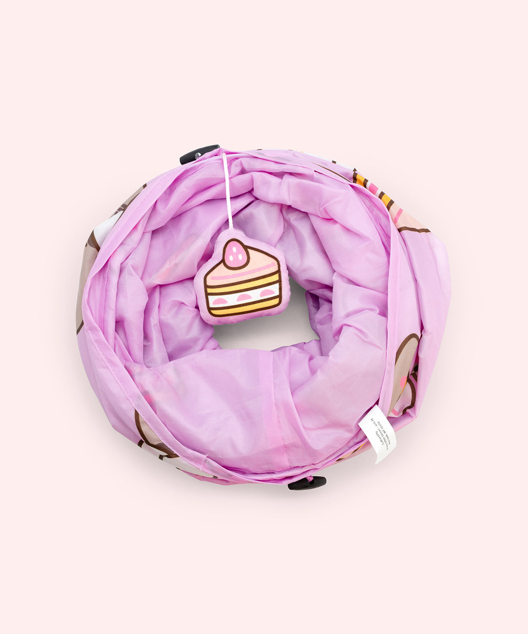 Collapsed view of the pet tunnel that has a plush dangle of a slice of strawberry cake on one end.