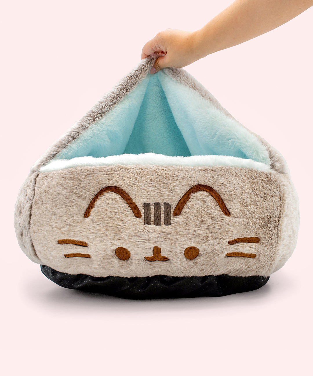 Plush cat-shaped pet bed with a hand holding the top open to reveal the light blue interior lining.