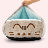 Plush cat-shaped pet bed with a hand holding the top open to reveal the light blue interior lining.