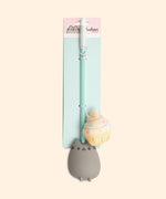 Pusheen Cat Teaser toy in packaging. The toy stick is attached to a backing card in two places. The long white string is wrapped around the mint green stick and the plush cupcake sits next to the Pusheen molded handle. The backing card is two-toned pink and mint-green and states "Pusheen the Cat, Cupcake Cat Teaser.” 