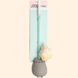 Pusheen Cat Teaser toy in packaging. The toy stick is attached to a backing card in two places. The long white string is wrapped around the mint green stick and the plush cupcake sits next to the Pusheen molded handle. The backing card is two-toned pink and mint-green and states "Pusheen the Cat, Cupcake Cat Teaser.” 