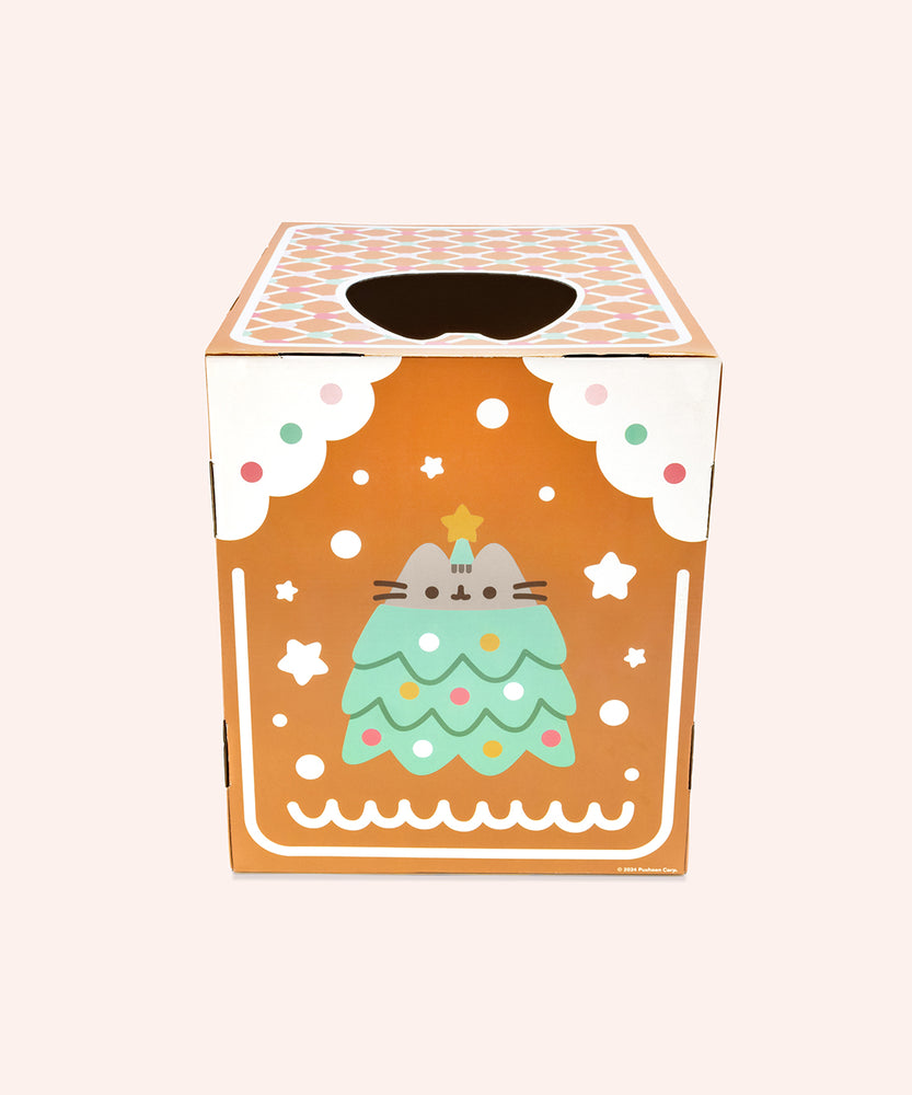 Back view of the cardboard box scratcher. The gingerbread house has white piping details and a graphic of Pusheen wearing a decorated christmas tree costume surrounded by snow stars.