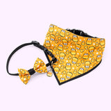 Front view of Pusheen Pet Halloween Candy Collar & Bandana Set. The black collar has an attached bowtie with an all over print of orange, white, and yellow candy corns and a Pusheen Candy Corn charm. The bandana has an orange background and an all-over-print graphic of Pusheen as a striped candy corn surrounded by more candy corn and white stars. 