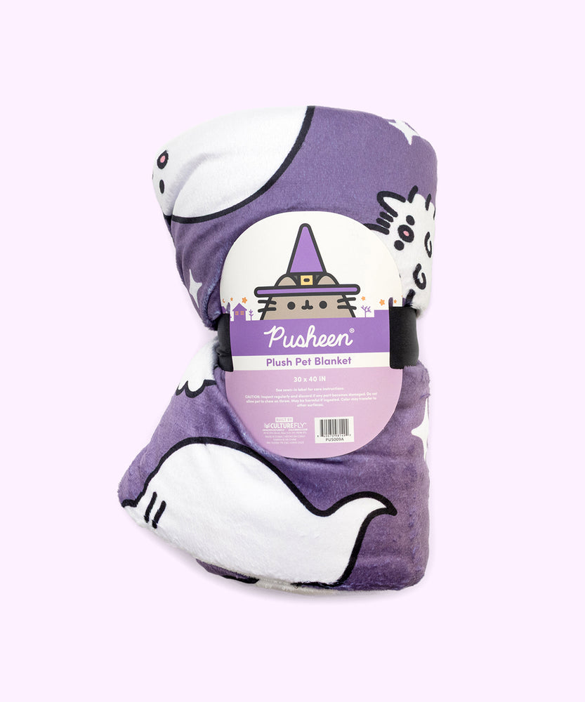 The Halloween Pet blanket is rolled inside its packaging which states that it is a “Pusheen Plush Pet Blanket.” The packaged black blanket sits in front of a light purple background. 