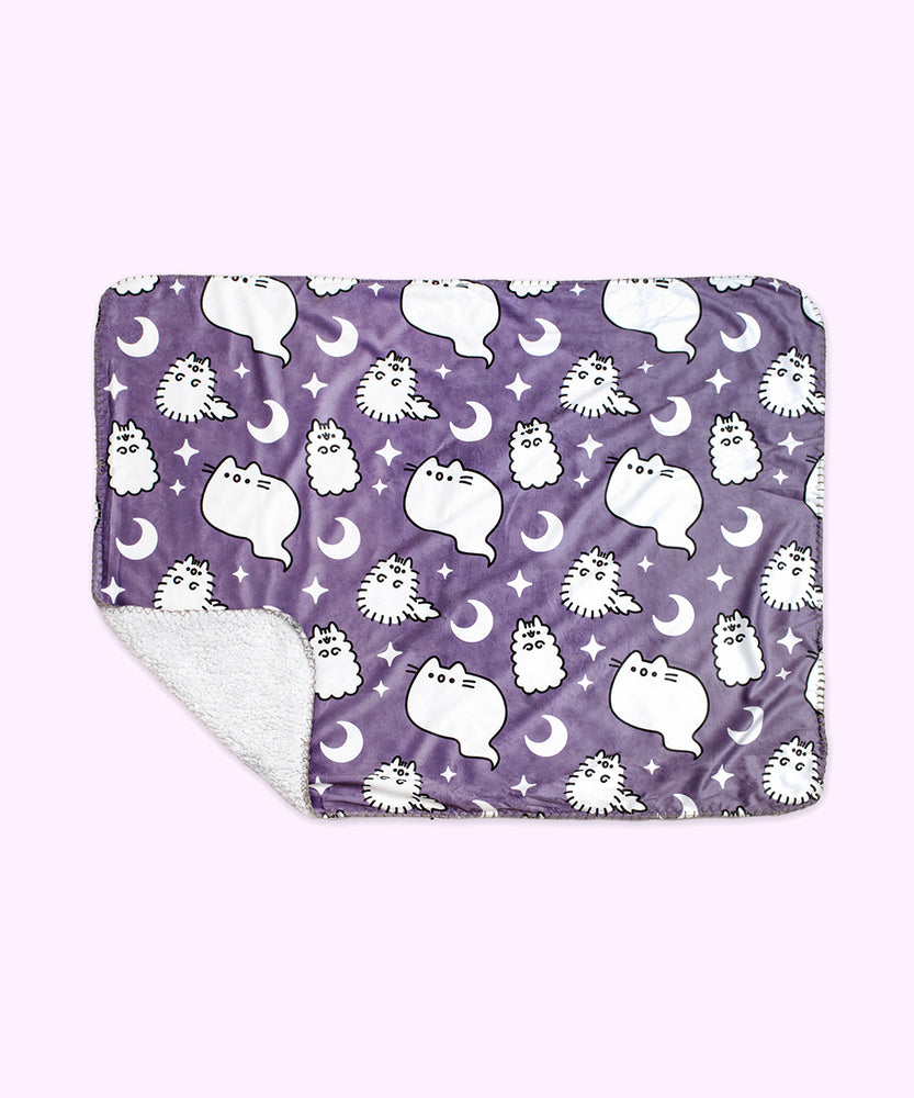 The Halloween Pet blanket is rolled inside its packaging which states that it is a “Pusheen Plush Pet Blanket.” The packaged black blanket sits in front of a light purple background. 