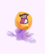 Close-up of the orange ball plush pet toy with purple feathers attached to the bottom. The print on the ball features Vampurr Pusheen and says "spooky cutie."