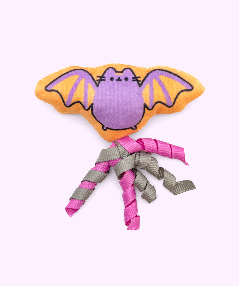 Close-up of the orange and purple bat-shaped plush pet toy with pink and grey ribbons attached to the bottom. 