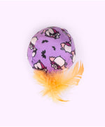 Close-up of the purple ball plush pet toy with orange feathers attached to the bottom. The all over print on the ball features Vampurr Pusheen and black bats.