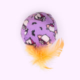 Close-up of the purple ball plush pet toy with orange feathers attached to the bottom. The all over print on the ball features Vampurr Pusheen and black bats.