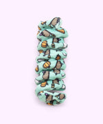 Close-up of mint green spiral cat toy that has a pattern of Witchsheen wearing a purple hat and riding a broom surrounded by pumpkins and ghosts.