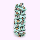 Close-up of mint green spiral cat toy that has a pattern of Witchsheen wearing a purple hat and riding a broom surrounded by pumpkins and ghosts.