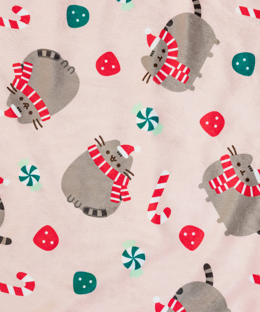 Close-up view of the all over graphic print on the main side of the pet blanket. Pusheen is shown in two poses, one sitting and smiling and one standing. In both poses, the grey tabby cat wears a red and white striped scarf and hat.