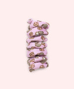 Close-up of purple spiral cat toy that has a pattern of Pusheen the Cat blushing while wearing whipped cream on her head with a tiered strawberry cake slice.